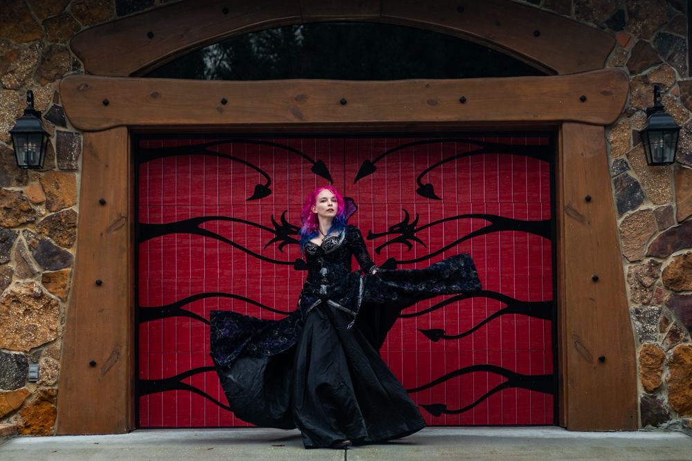 A figure in a black costume with flowing fabric performs a dramatic pose in front of a red door.