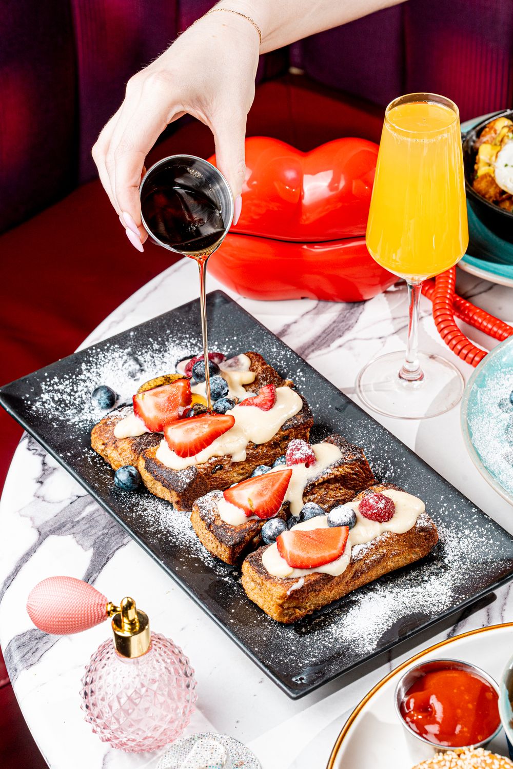 French toast topped with berries and cream on a black plate, with syrup being poured over it.