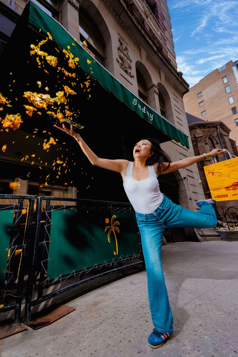 A joyful woman tosses golden confetti outside an Inday restaurant in New York City.