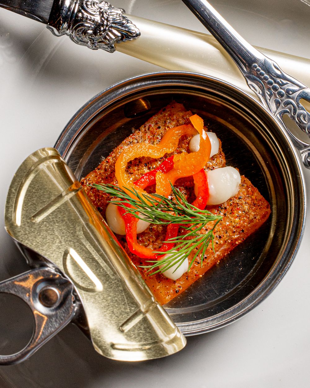 Gourmet dish served in an open tin can with roasted peppers and fresh rosemary garnish.