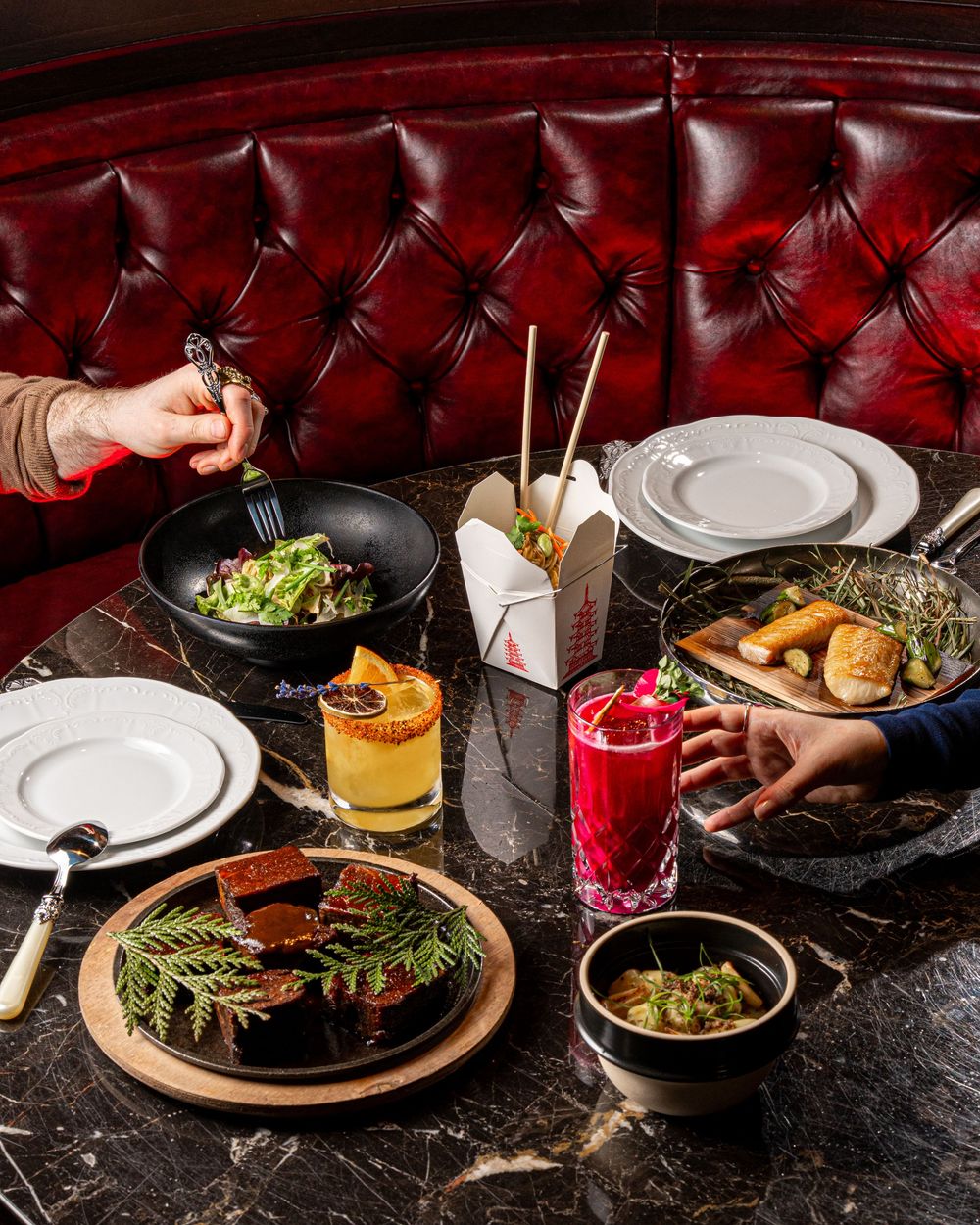 An elegant restaurant table with salads, cocktails, and appetizers on a marble surface with red leather seating.
