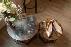 Wedding detail flat lay with invitation cards, bridal shoes, and floral arrangements on wooden floor.