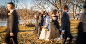 Motion-blurred wedding party stands in front of a lake during golden hour at sunset.
