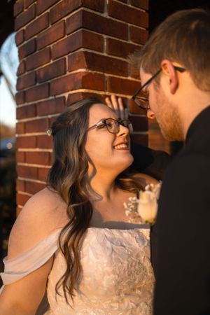 Intimate moment between couple by brick wall during wedding photoshoot.