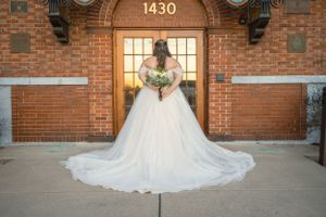 Bride in flowing white gown poses in front of brick building entrance with address 1430.