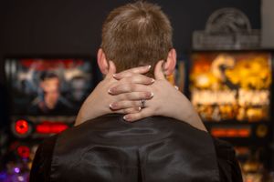 Back view of someone wearing a ring and leather jacket in front of illuminated displays.