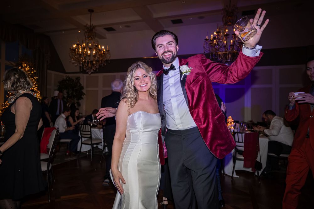 Reception guests dance energetically on a ballroom floor under decorative chandeliers during a wedding celebration.