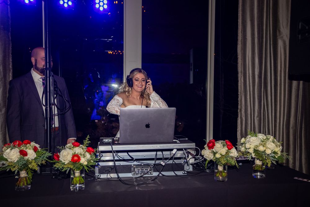 DJ plays music at a wedding reception with blue lighting and floral decorations on tables.