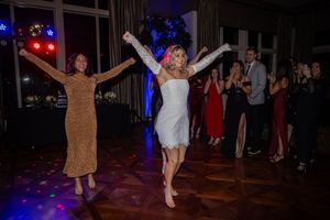 Party guests dance energetically on a dark dance floor illuminated by colorful disco lights in an indoor venue.