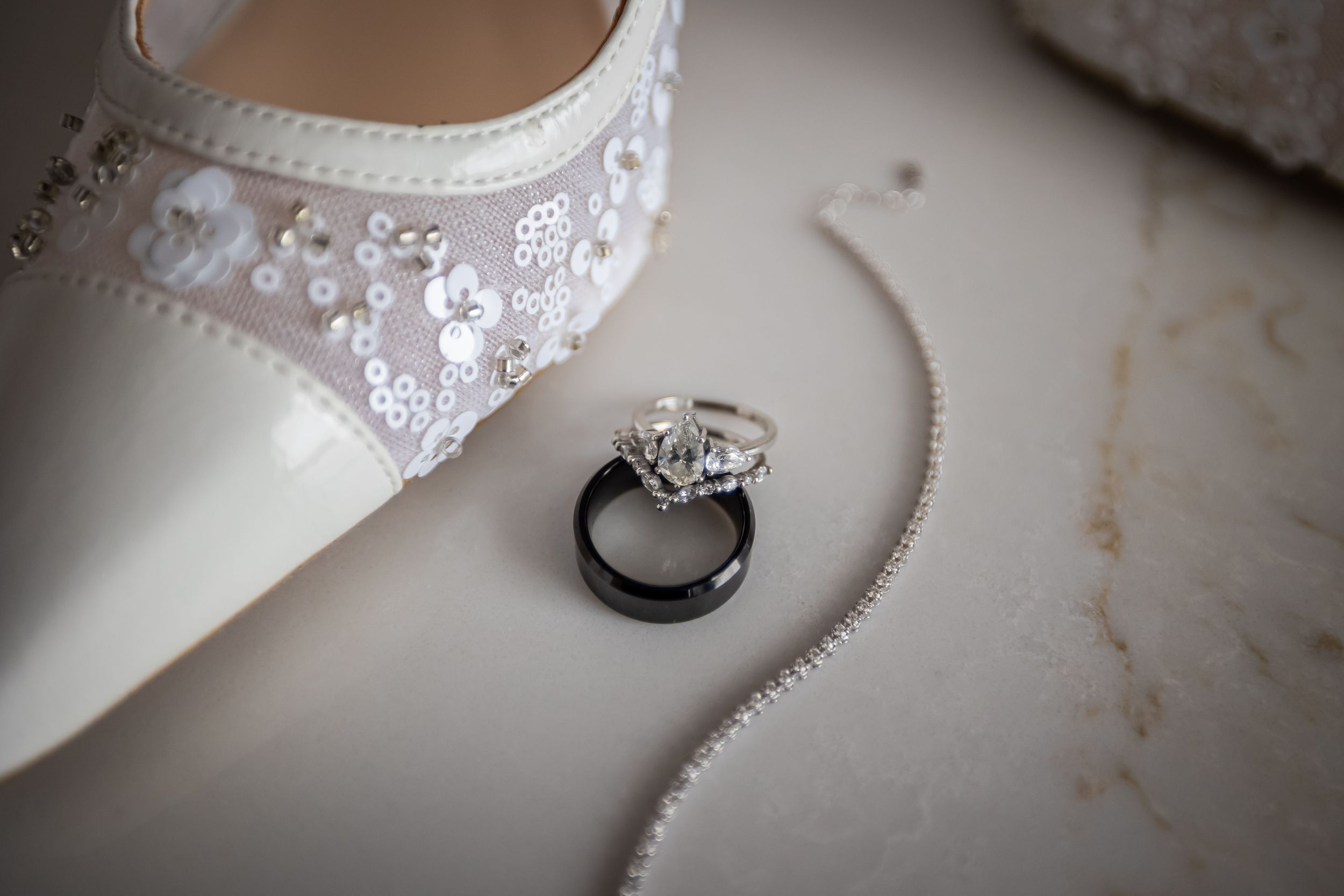 Elegant white lace bridal shoe with diamond engagement ring on light background.