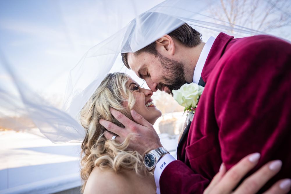 Newlywed couple shares a romantic kiss under a flowing veil on their winter wedding day.