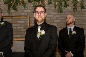 Formal black and white photo of groomsmen in tuxedos at a wedding with brick wall background.
