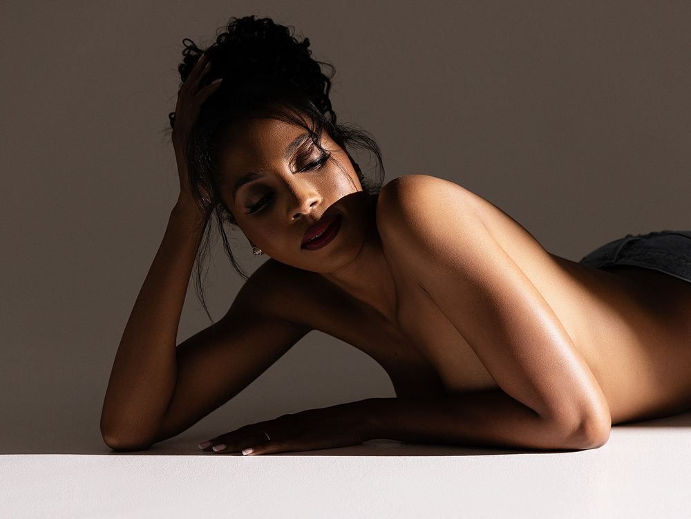 A person lies on their side in an artistic boudoir portrait with soft dramatic lighting against a dark background.