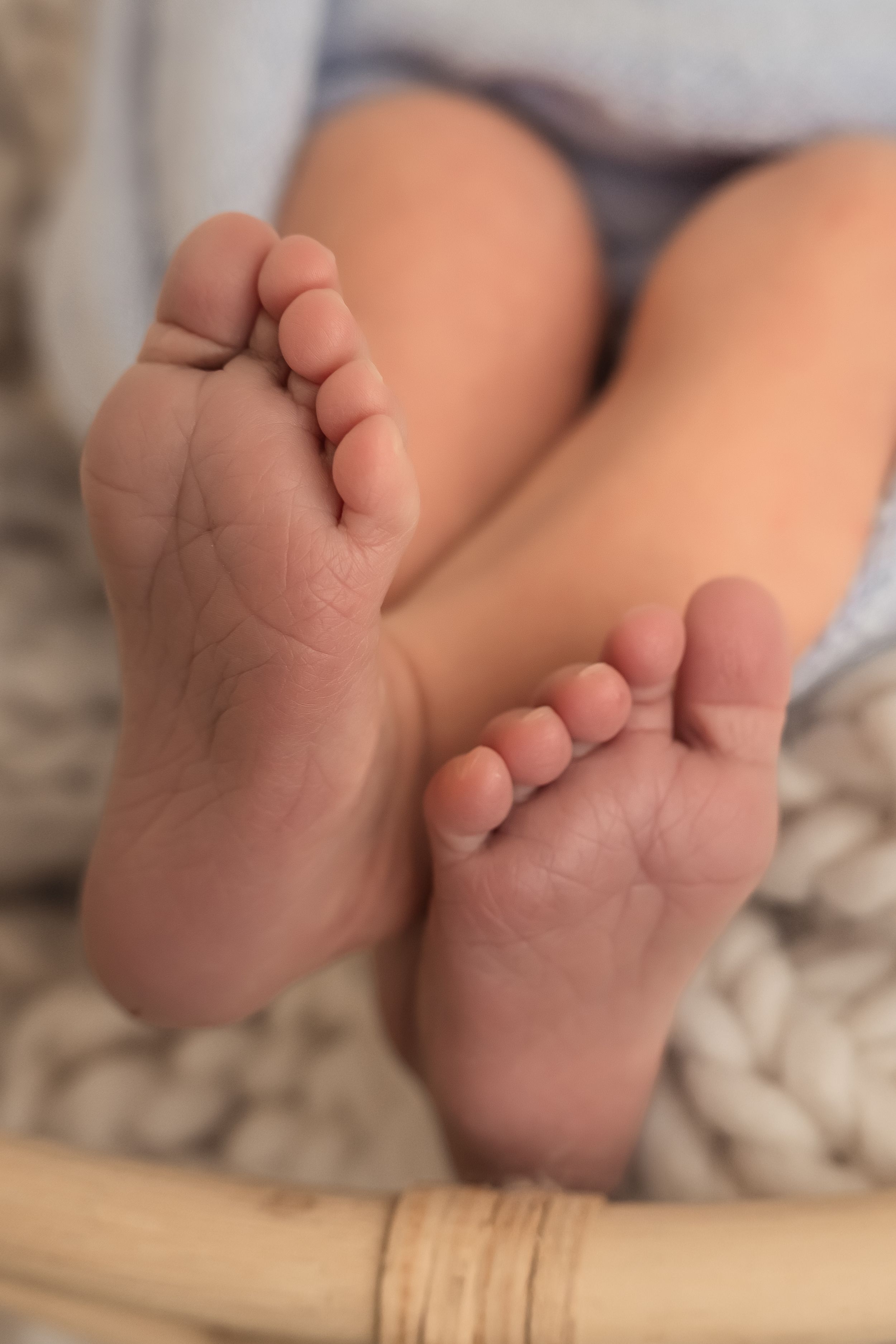 Close-up of small baby feet with tiny toes resting on a soft knit blanket in a wicker basket.
