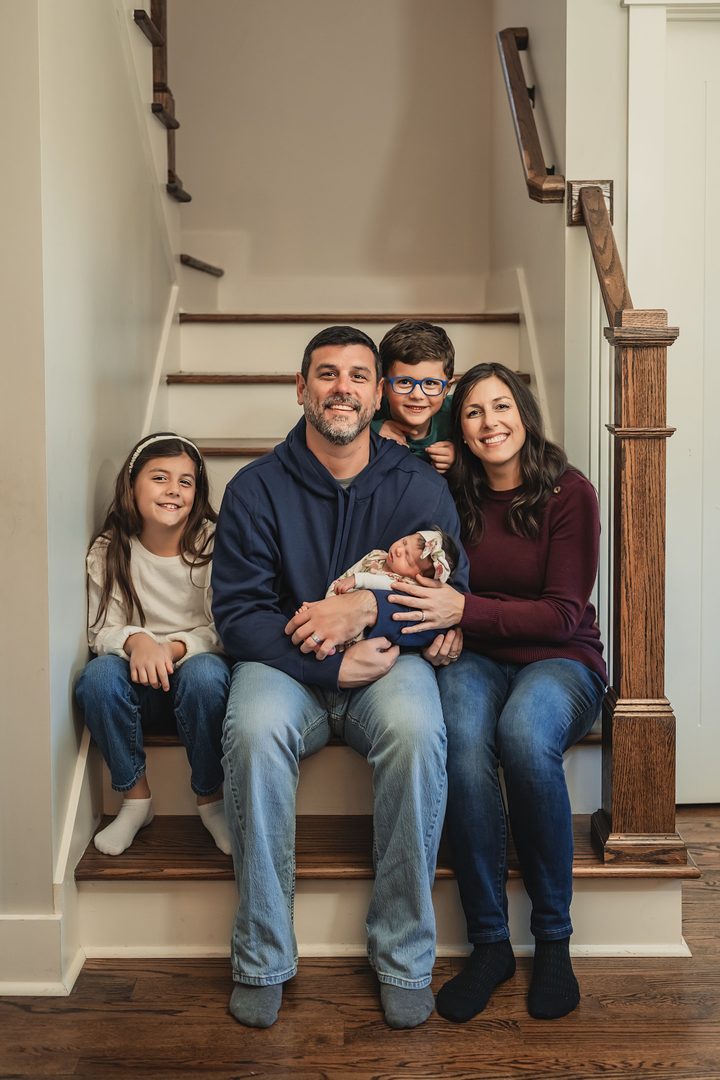 A loving family sits together on their stairs while holding their newborn daughter in their home for newborn photos in Chattanooga.