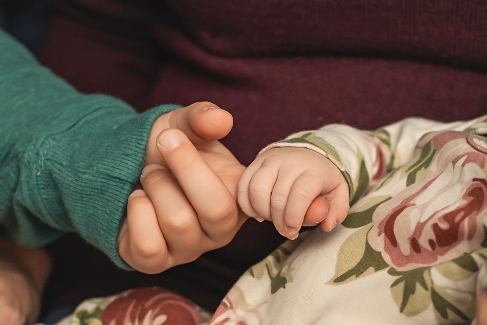 A small baby's hand grasps her big brother's finger at lifestyle newborn photo session in Chattanooga
