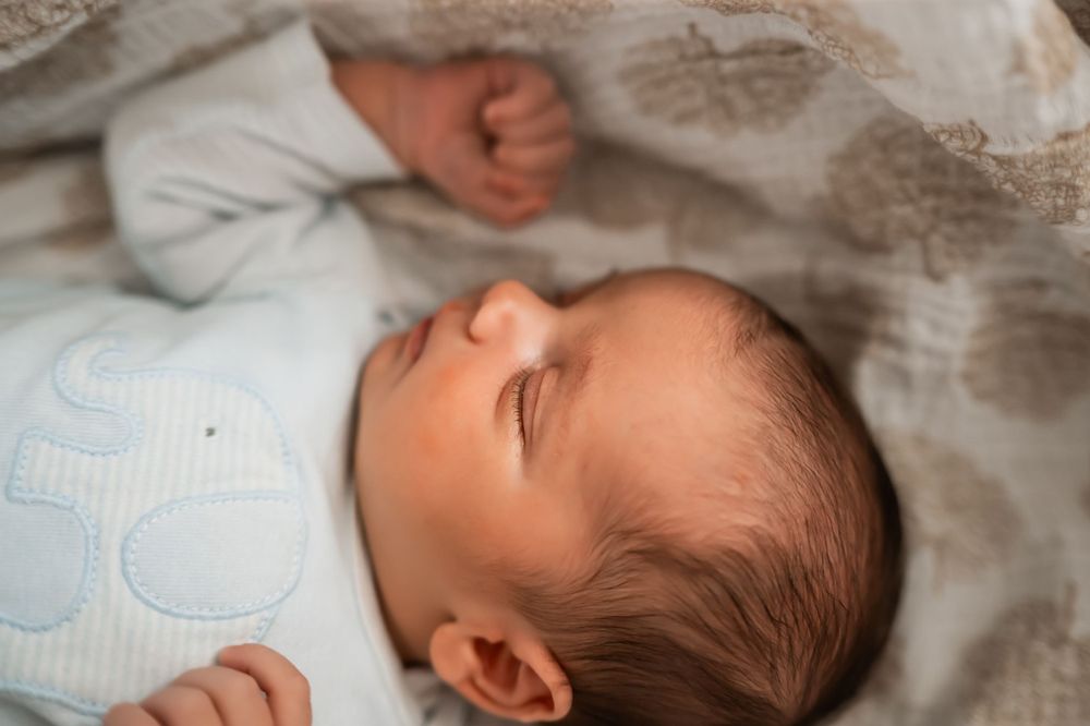 A sleeping baby lies peacefully on light blue and white bedding with soft brown hair visible.