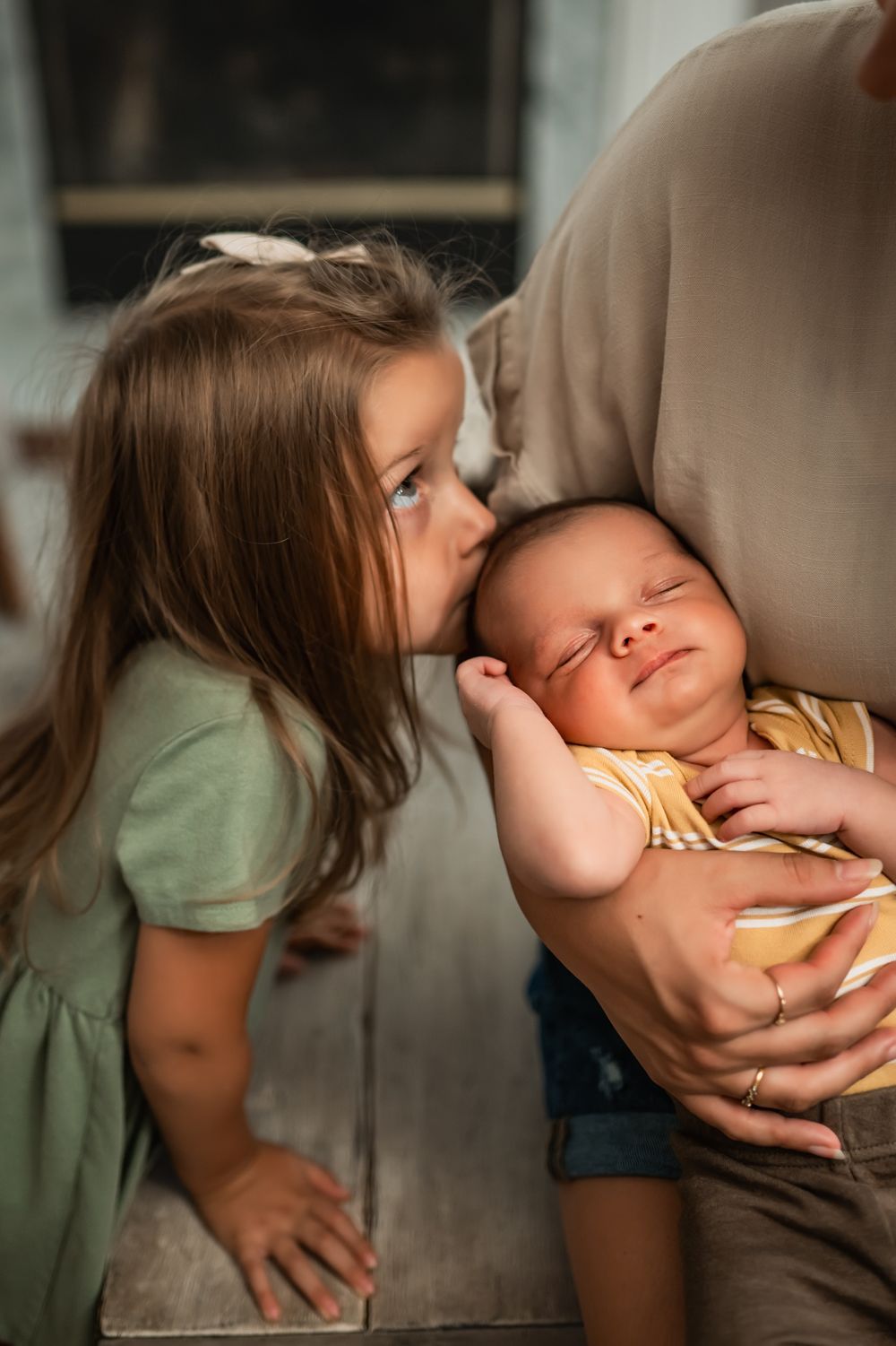 A touching scene as a young girl gives a gentle kiss to her sleeping baby brother held warm in Dad's arms.