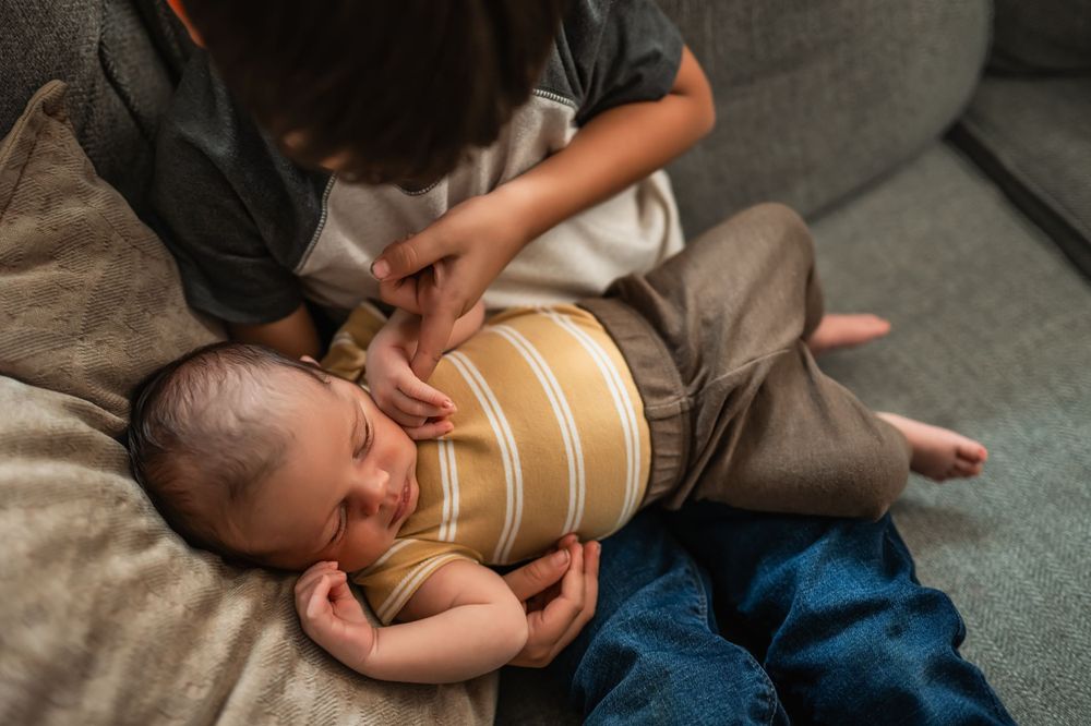 Big brother holds newborn baby brother on the couch for lifestyle newborn photos in their family home.