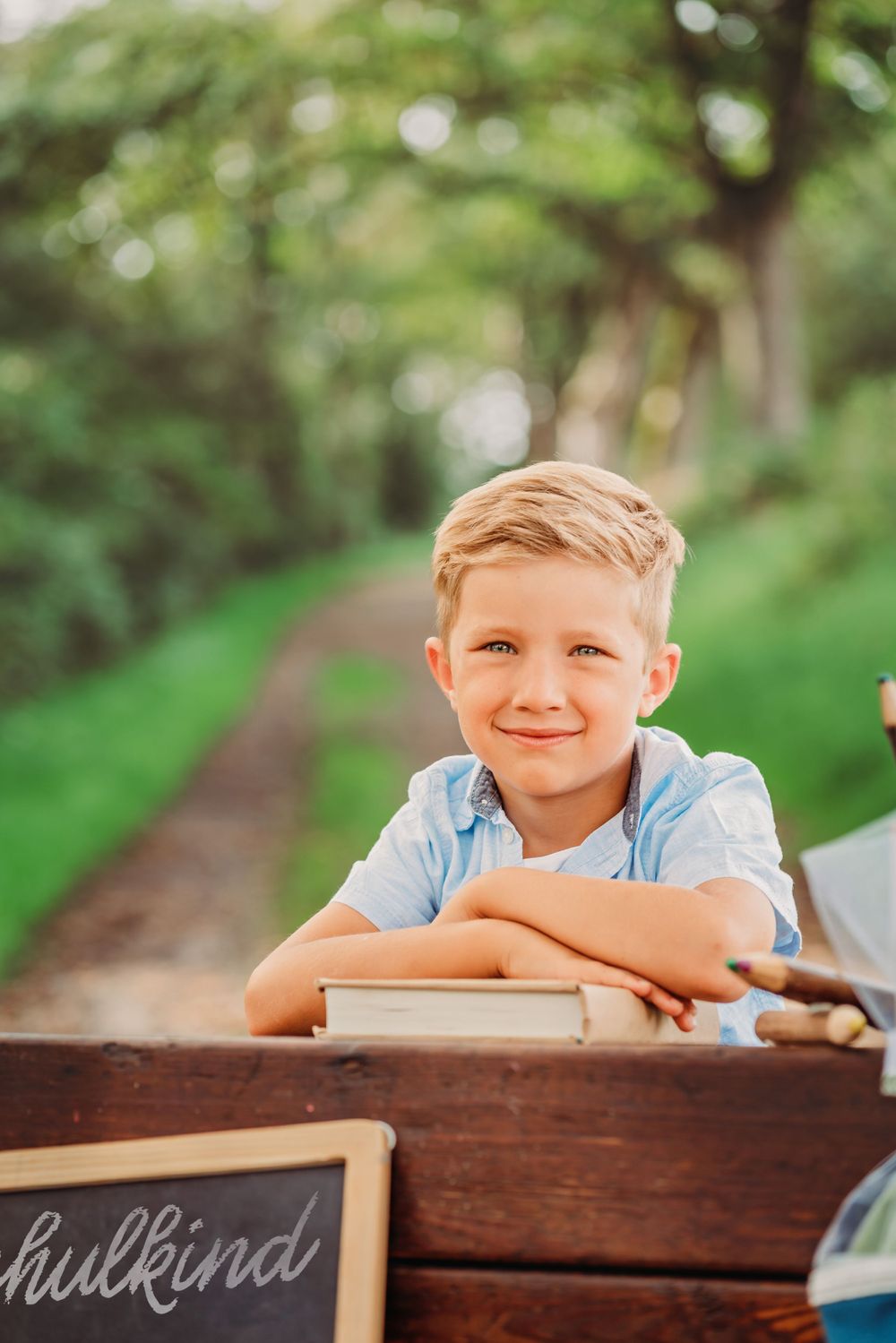 Young student leaning on vintage wooden desk outdoors in wooded setting.