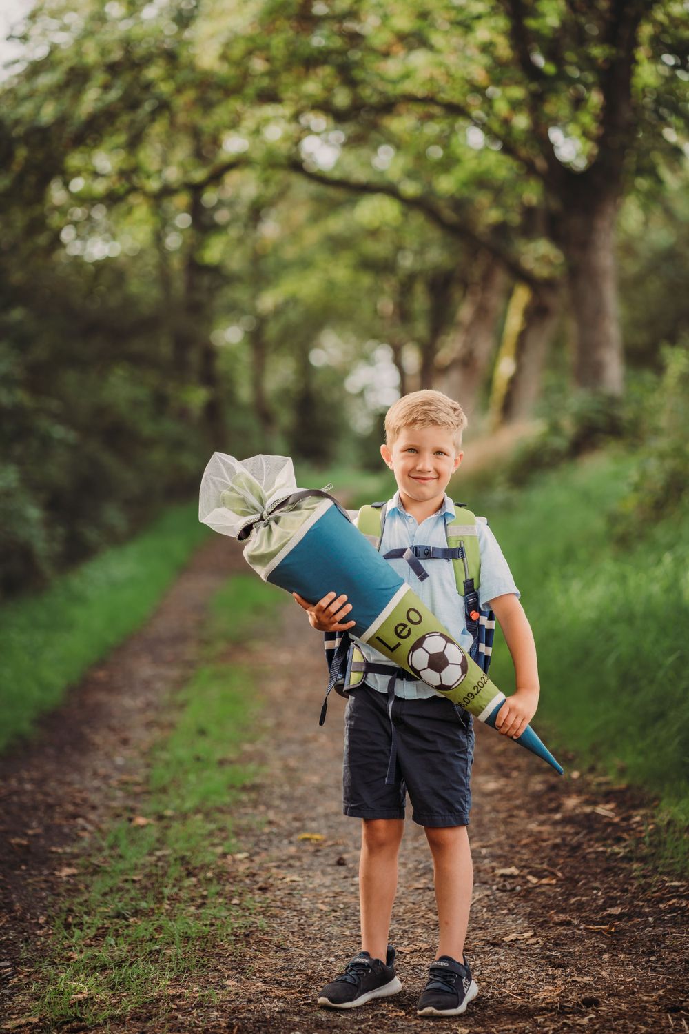 Child holding school supplies and soccer ball on forest trail.