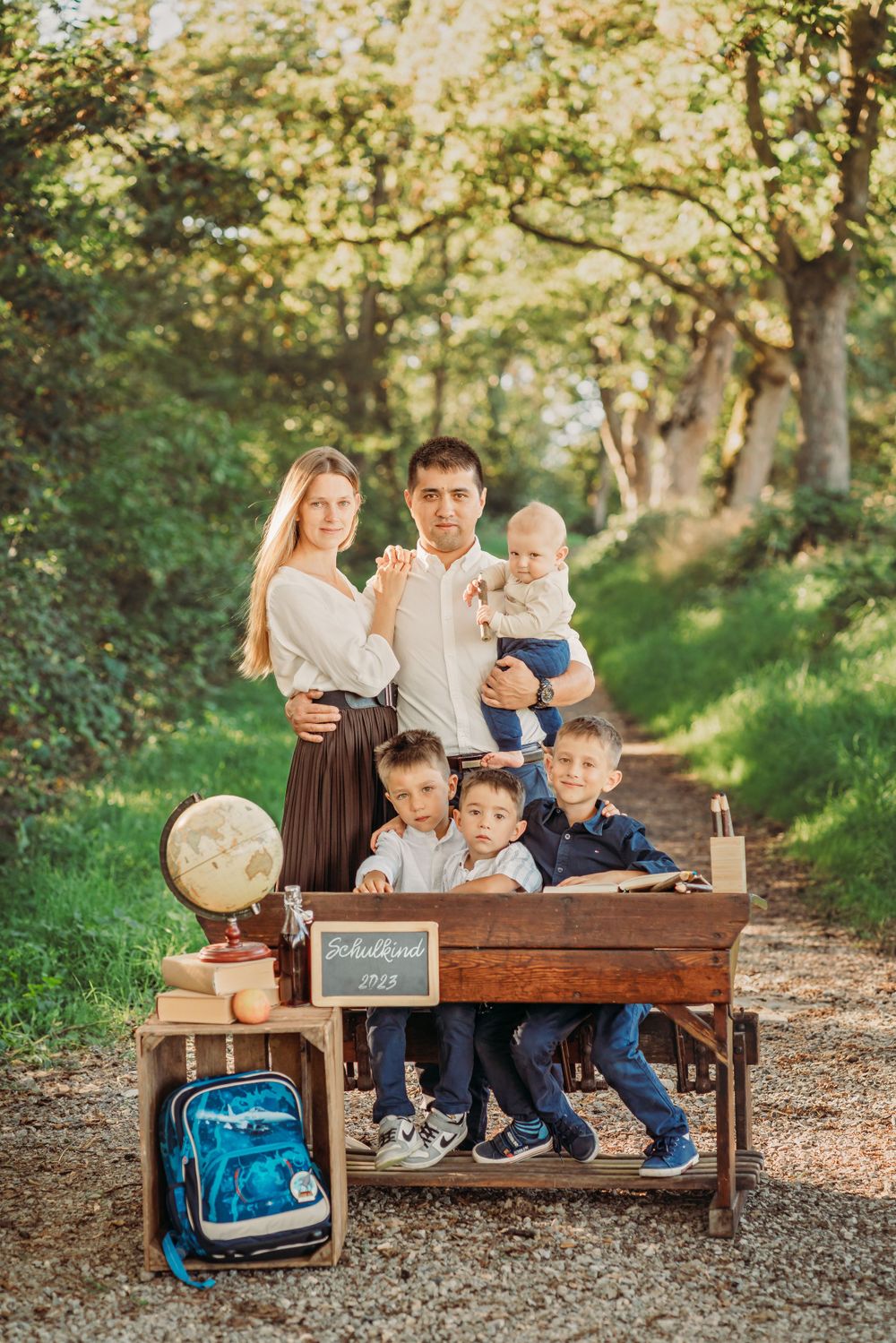 A family gathers around an antique desk in a forest setting for a back-to-school photo session.