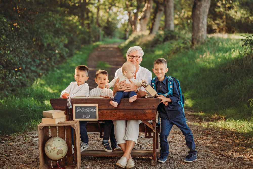 Multi-generational family gathering around vintage wooden desk on forest path.
