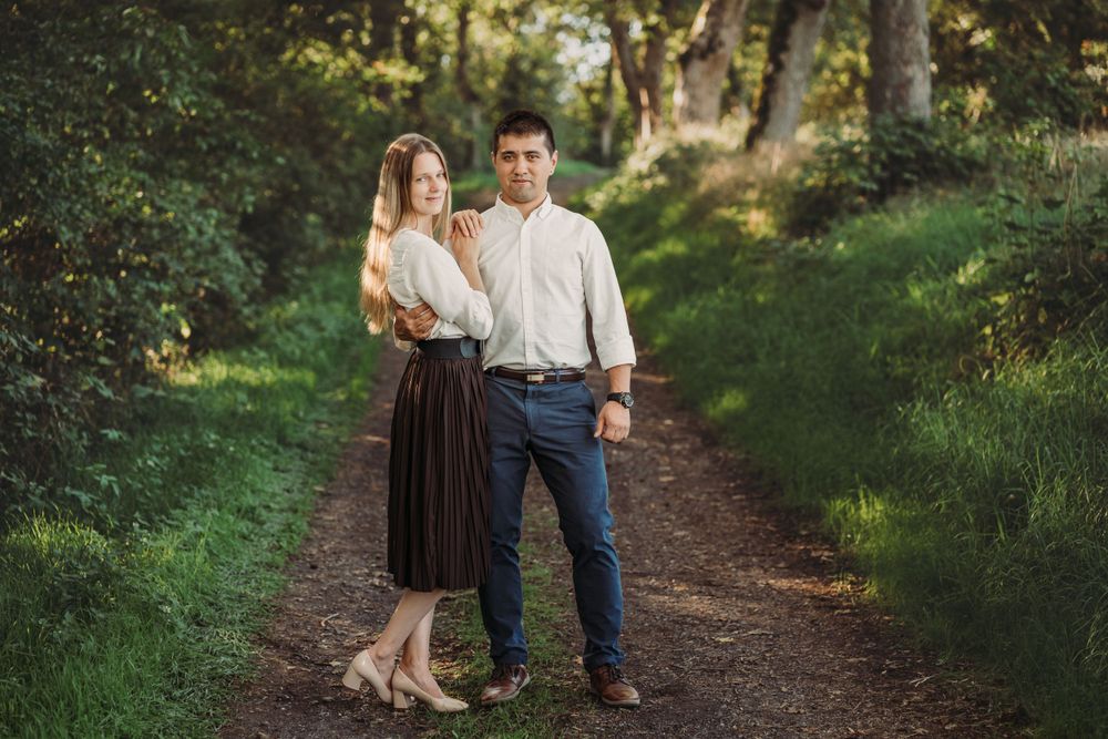 Romantic couple standing together on dirt path surrounded by lush green trees.