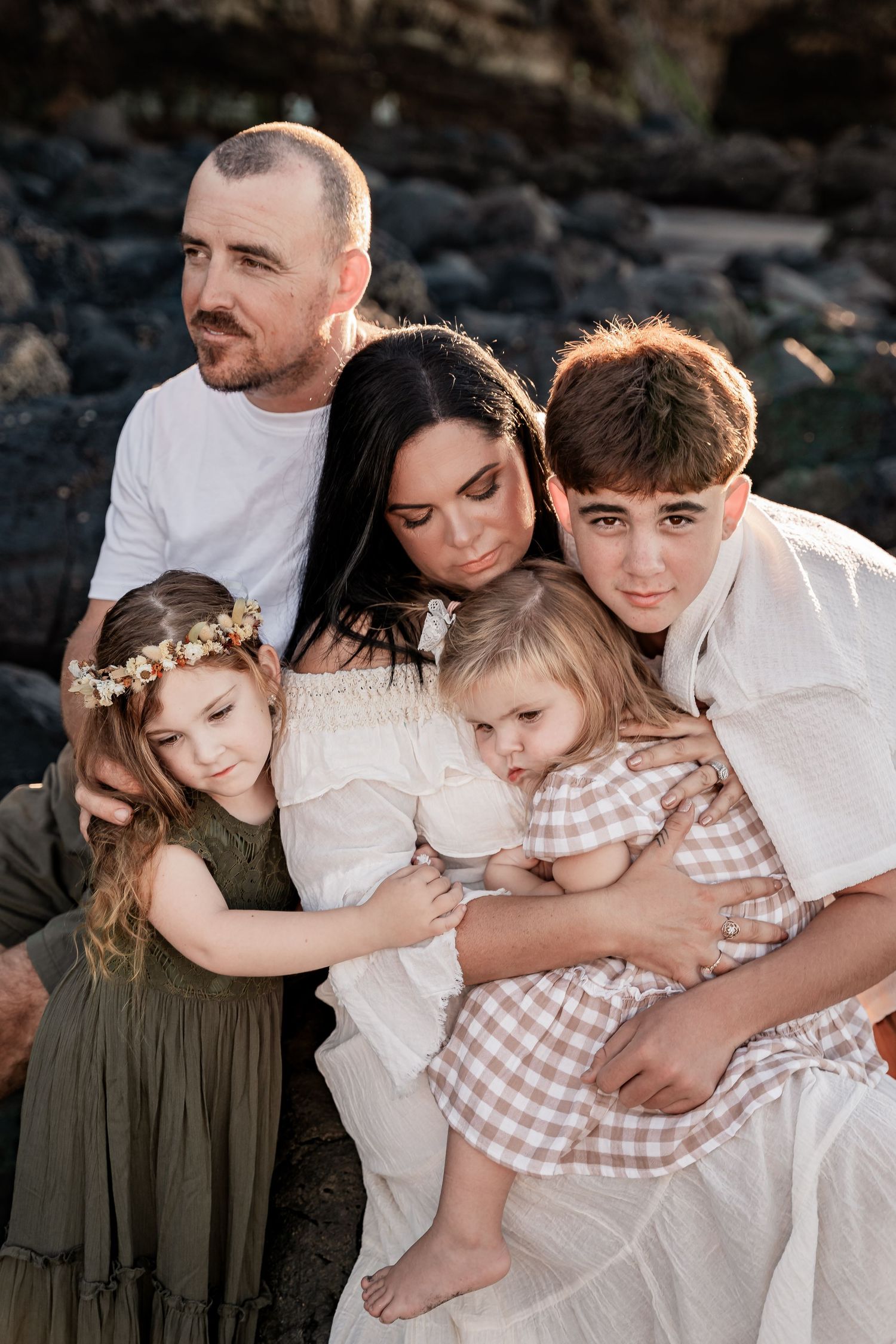 An intimate family portrait captured against rocky coastal backdrop.
