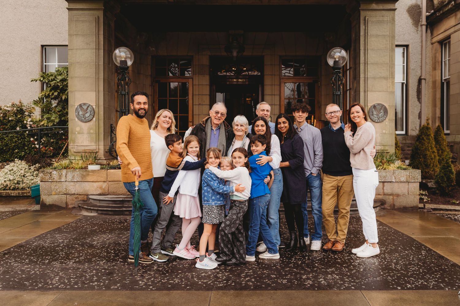 A large family group poses together for a portrait outside a grand stone building entrance.