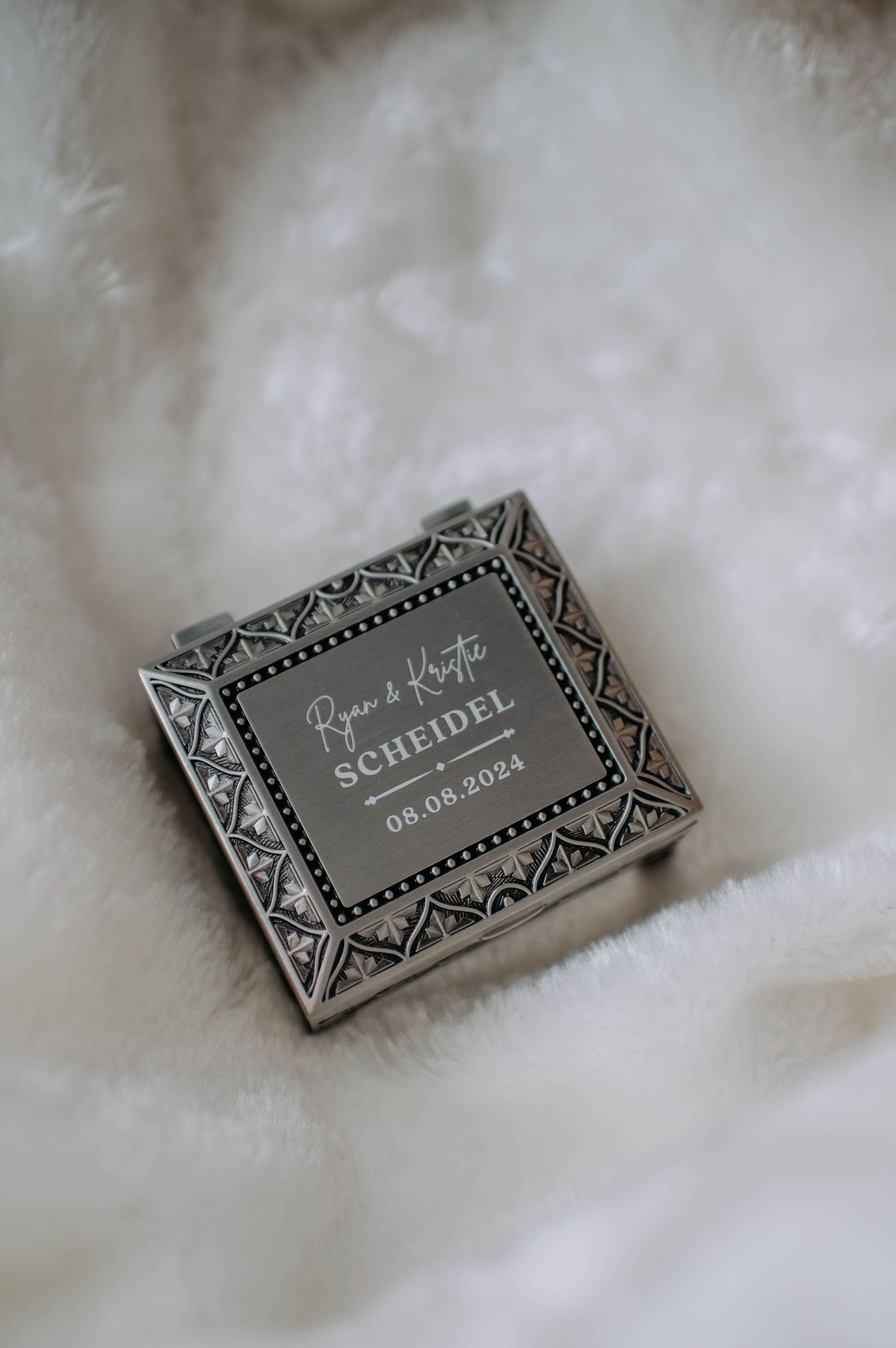 A geometric patterned wedding invitation box rests on a white fluffy surface.