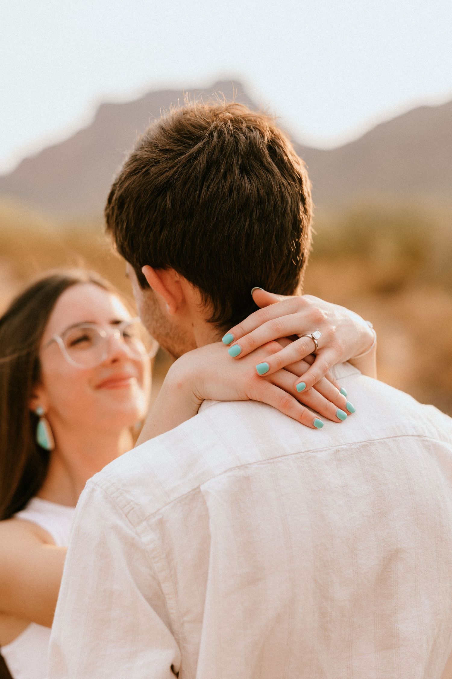 Romantic desert engagement photo showing ring display and embrace at sunset.