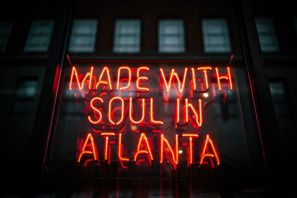 Red neon sign reading 'MADE WITH SOUL IN ATLANTA' glows against dark building with windows at night.