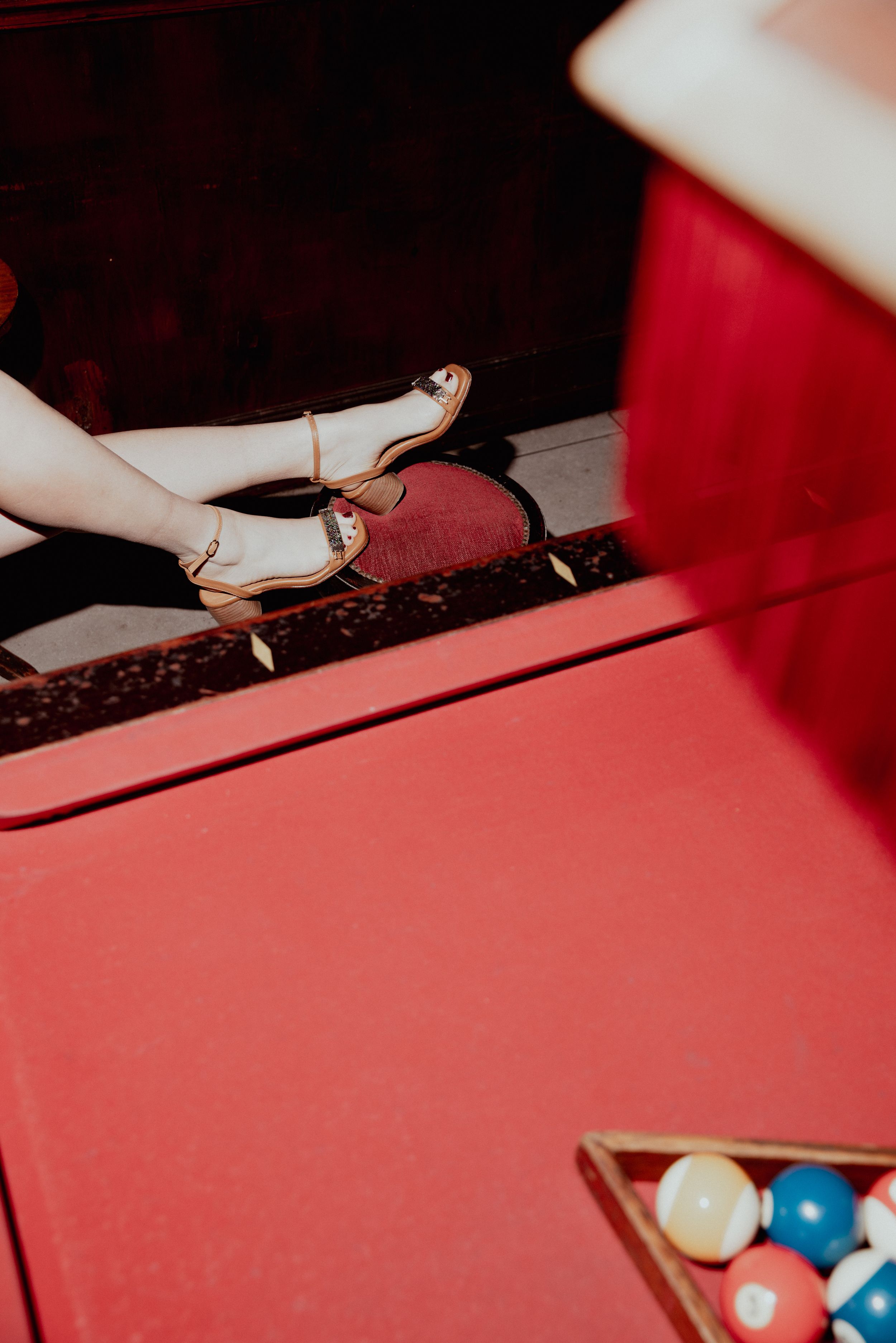 Red stiletto heels on a red pool table with billiard balls visible in the corner.
