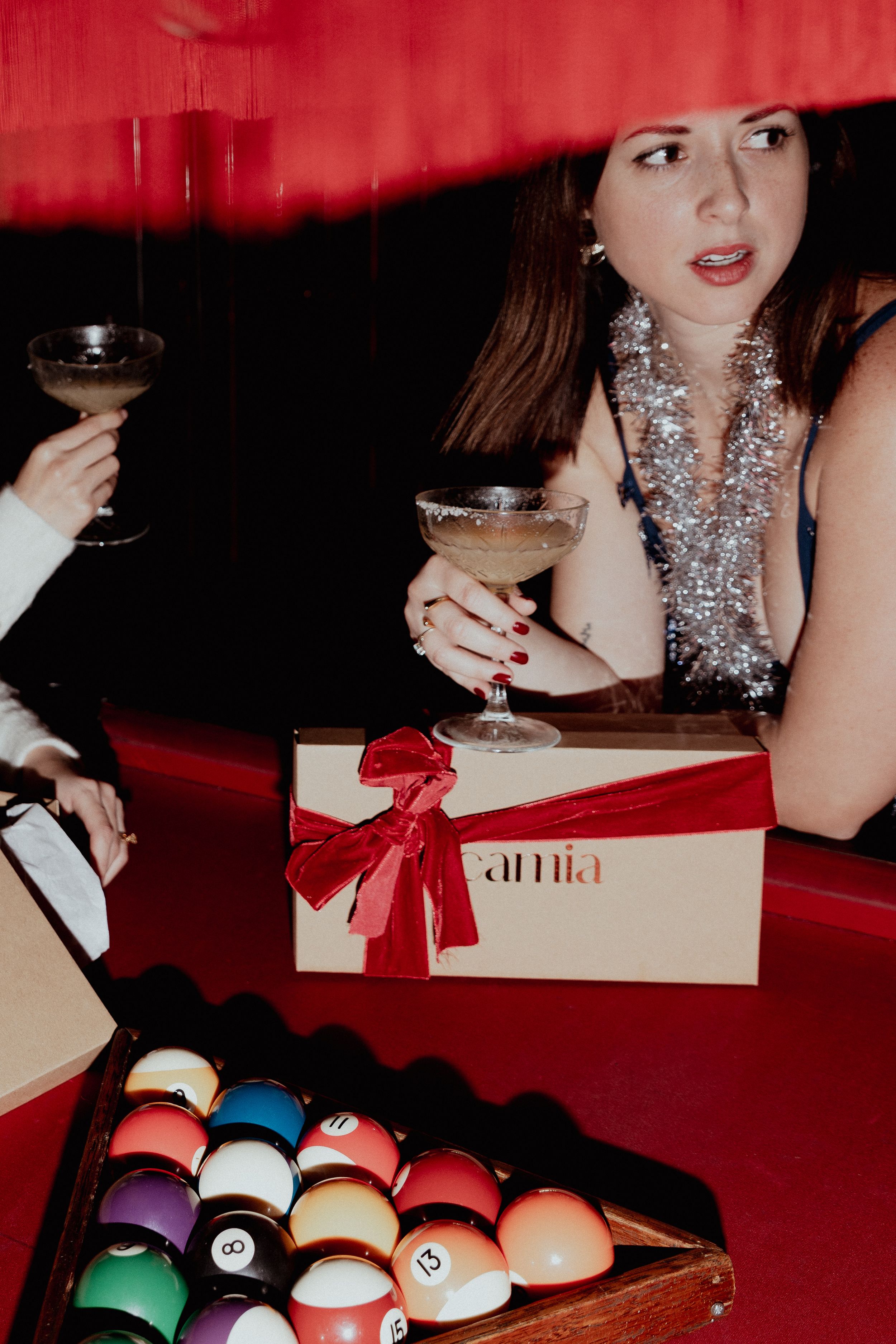 Cocktail glasses and colorful pool balls on a red felt table with silver tinsel decorations.