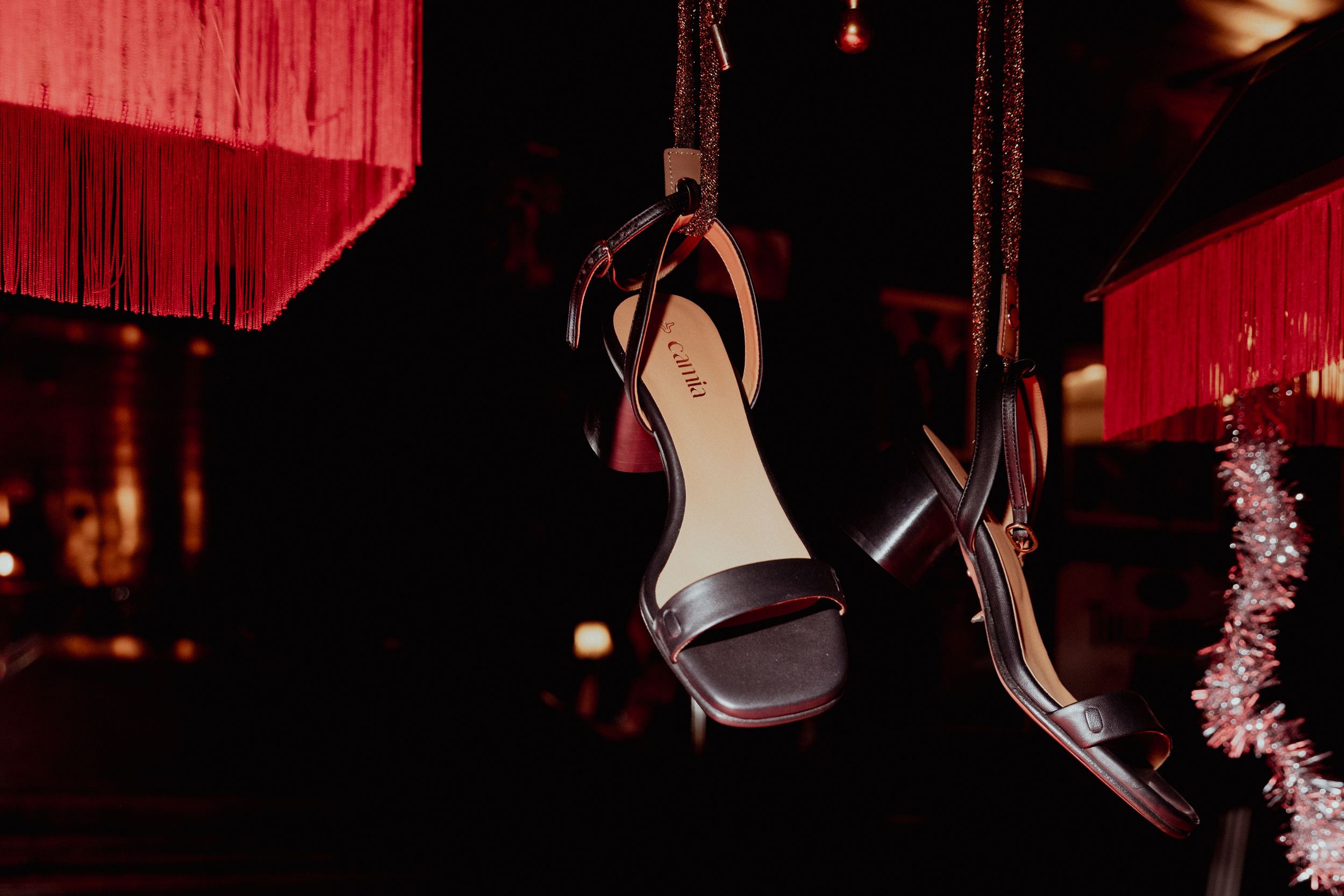 Dark elegant high heels hanging dramatically against red lighting.