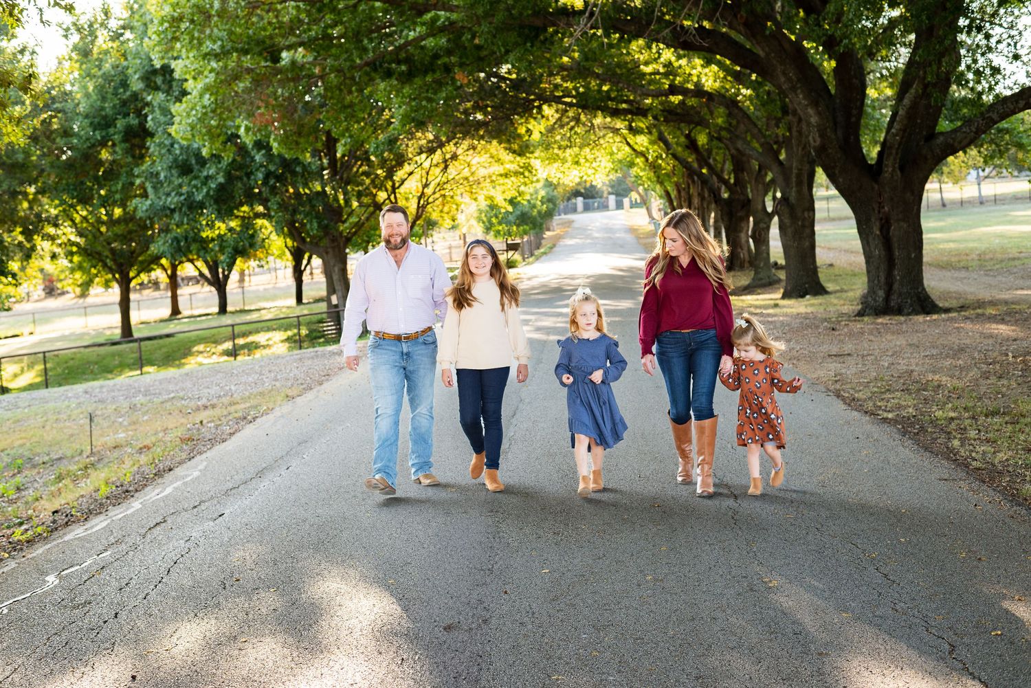 Family walking together on tree-lined path during golden hour.