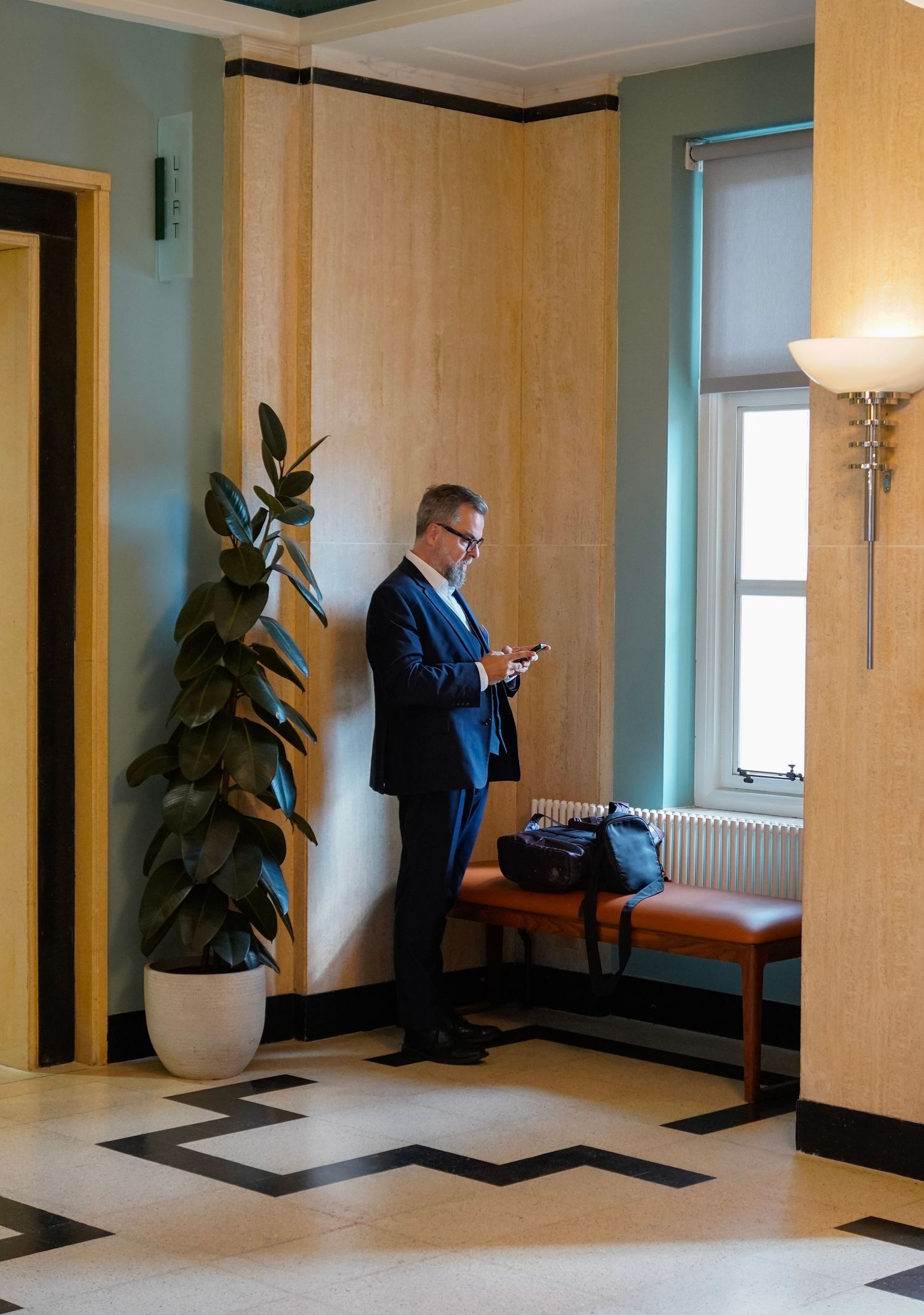Person in business suit checking phone in modern office lobby with geometric floor pattern.