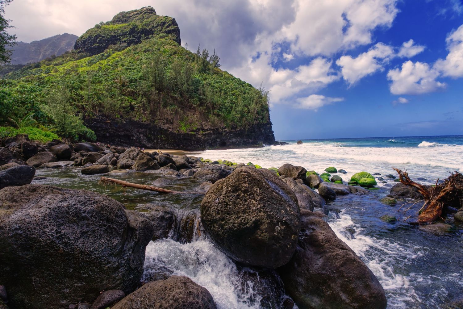 Beautiful blue sky with green lush mountains over rocky beach.