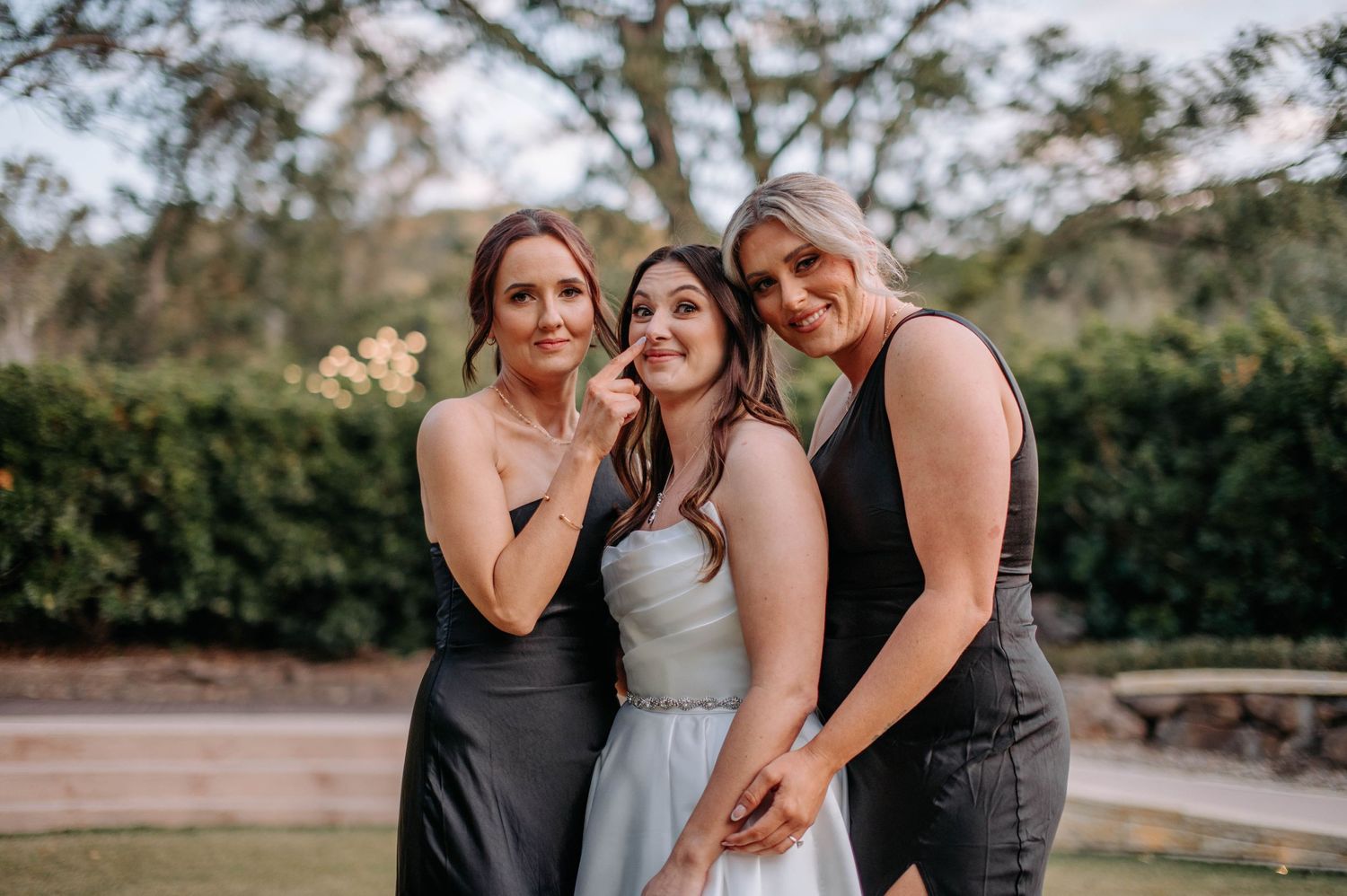 Three wedding attendants pose together outdoors in coordinated gray attire.