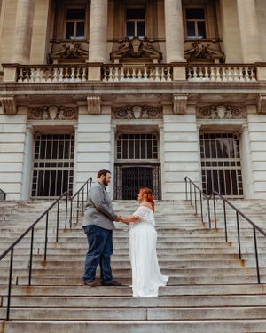 Wedding couple holding hands on historic building steps with ornate architectural details.