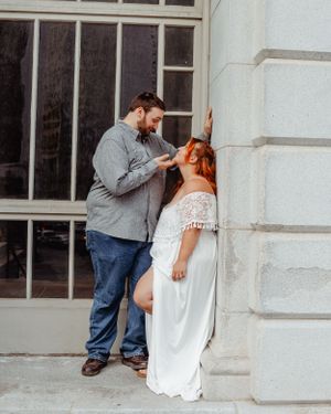 Romantic couple sharing an intimate moment against a white stone building wall.