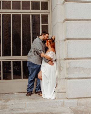 Tender moment between couple dressed in grey and white against stone building.