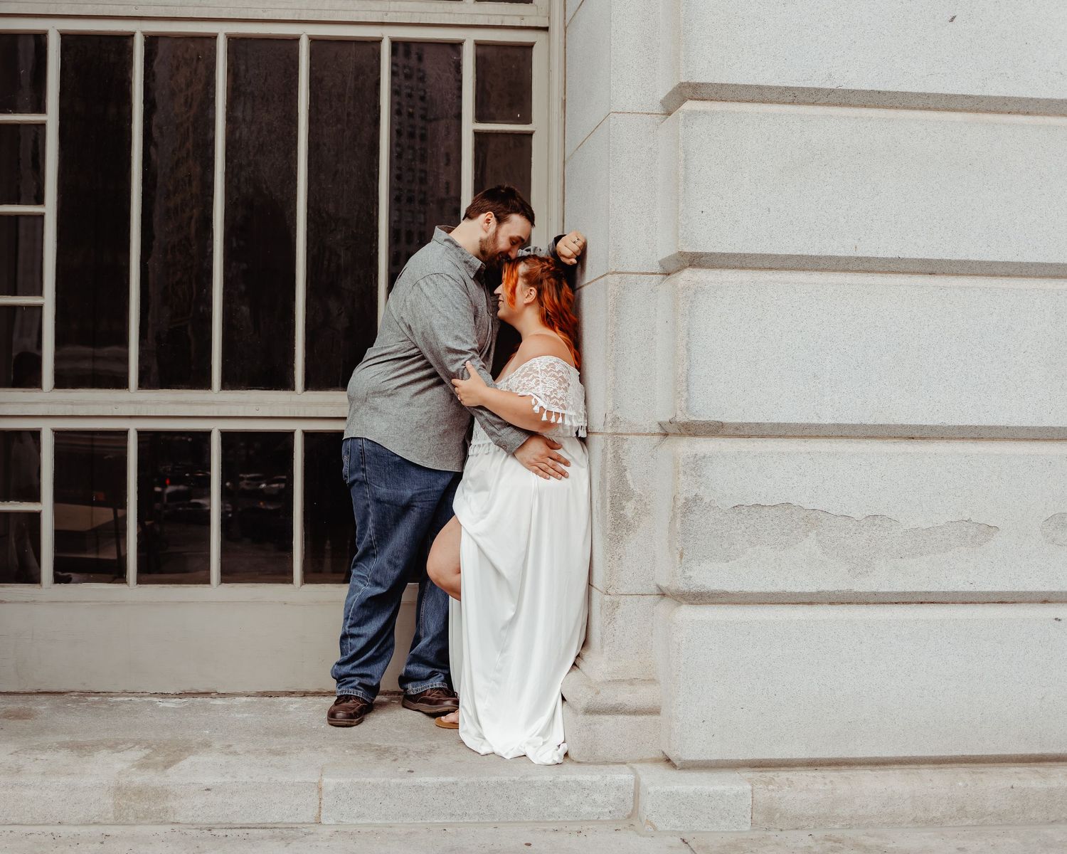 Intimate couple's photoshoot against urban stone wall with window backdrop.
