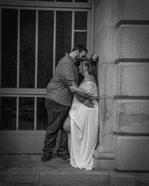 Black and white romantic portrait of couple embracing against stone building wall.