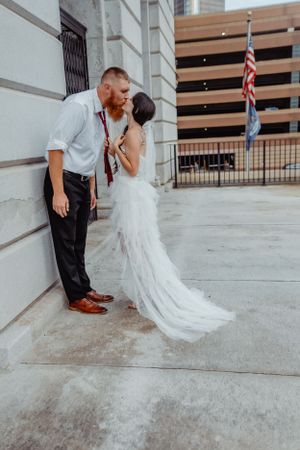 Bride and groom sharing intimate moment against urban building exterior.