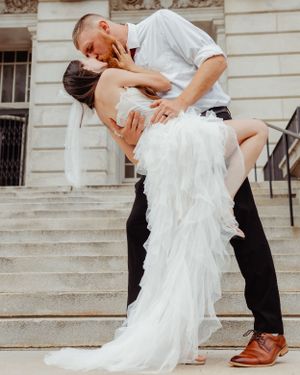 A dramatic wedding dip pose on historic building steps featuring a flowing white gown.