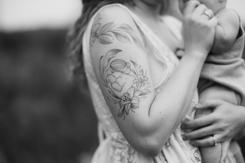 Close-up of a detailed floral tattoo on an arm holding a baby.