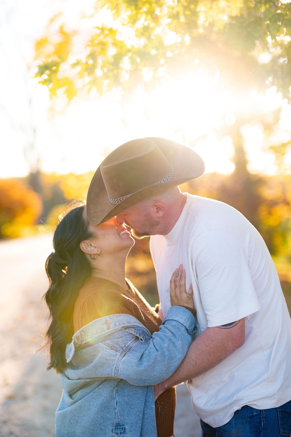A romantic sunset moment between a couple wearing casual clothes and a cowboy hat.