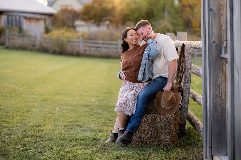 A couple embracing by a rustic wooden fence in countryside setting.